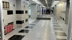 Moderni aula, jossa on kiillotettu kivilattia, vasemmalla puolella palosammutin ja keskellä lasihissi.