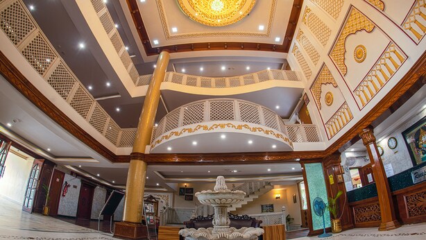 A grand lobby with a central fountain, ornate ceiling, and a staircase leading to an upper level. - NRS Royal Palace (Brahmagiri)
