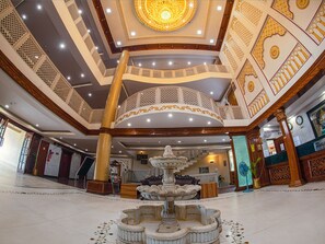 A grand lobby with a central fountain, ornate ceiling, and a staircase leading to an upper level. - NRS Royal Palace (Brahmagiri)