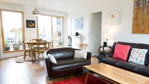 A living room with a brown leather sofa, a wooden coffee table, and a red rug. There is a dining area with a table and chairs, and a large window providing natural light. - ★ Beautiful Rooftop between Paris and Versailles ★ (Chaville)