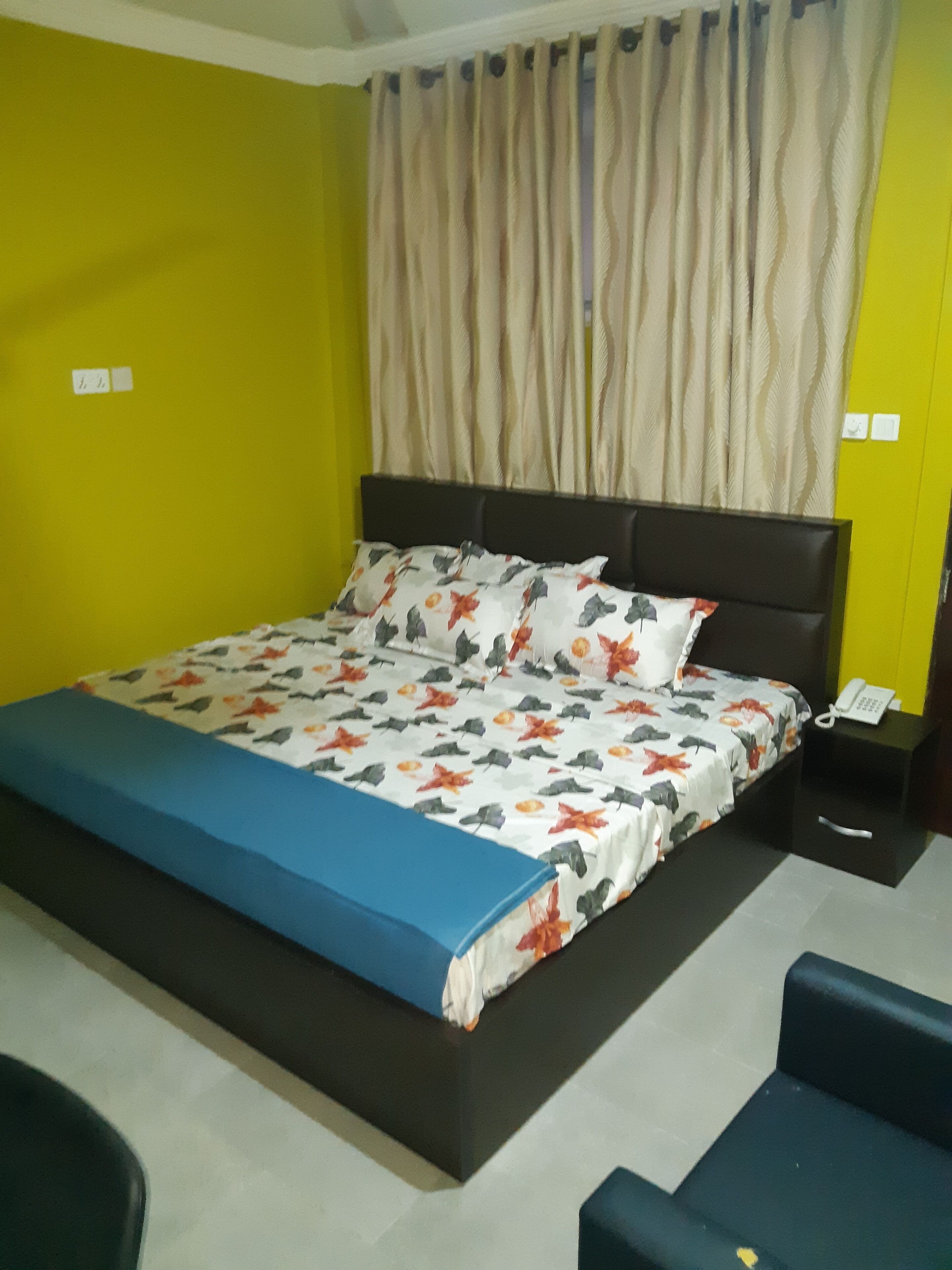 A hotel room with a large bed, a nightstand with a phone, and a chair.