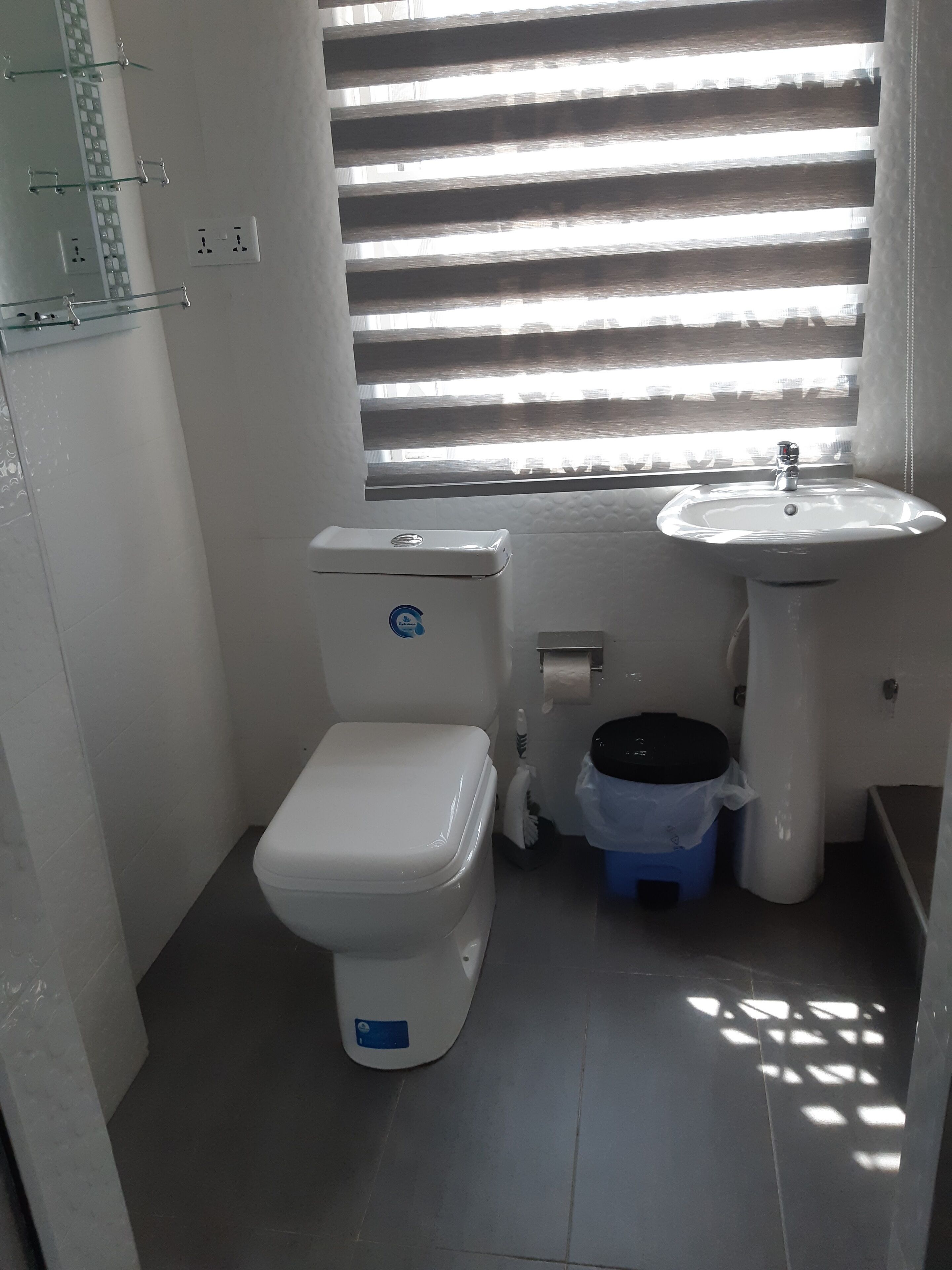 A small, clean bathroom with a toilet, sink, and window with blinds.