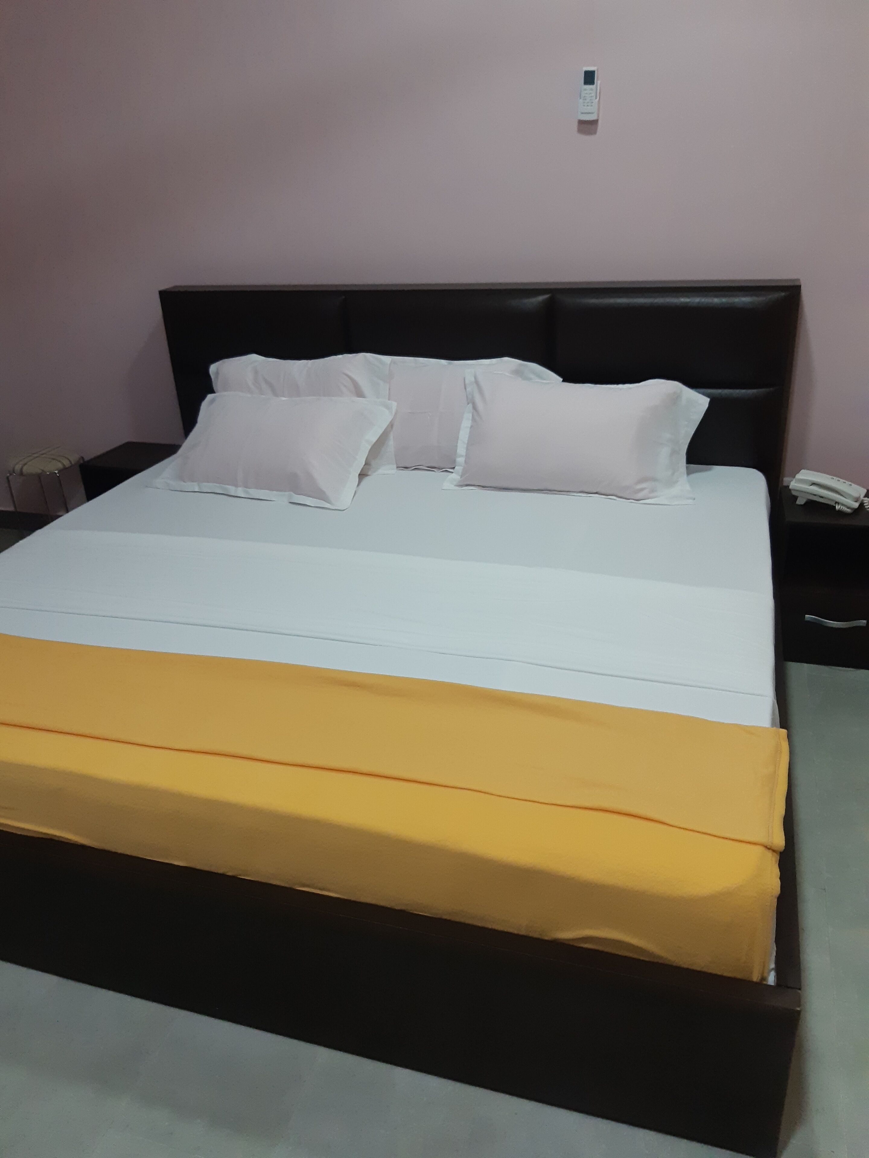 A bed with white and yellow bedding, a black headboard, and a bedside table with a phone.