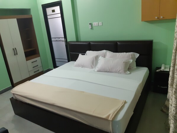 Una cama bien hecha con ropa blanca y almohadas, un cabecero negro y un armario con varias puertas y cajones.