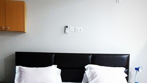 Una cama bien hecha con ropa blanca, un cabecero negro y una lámpara azul sobre una mesita de noche.