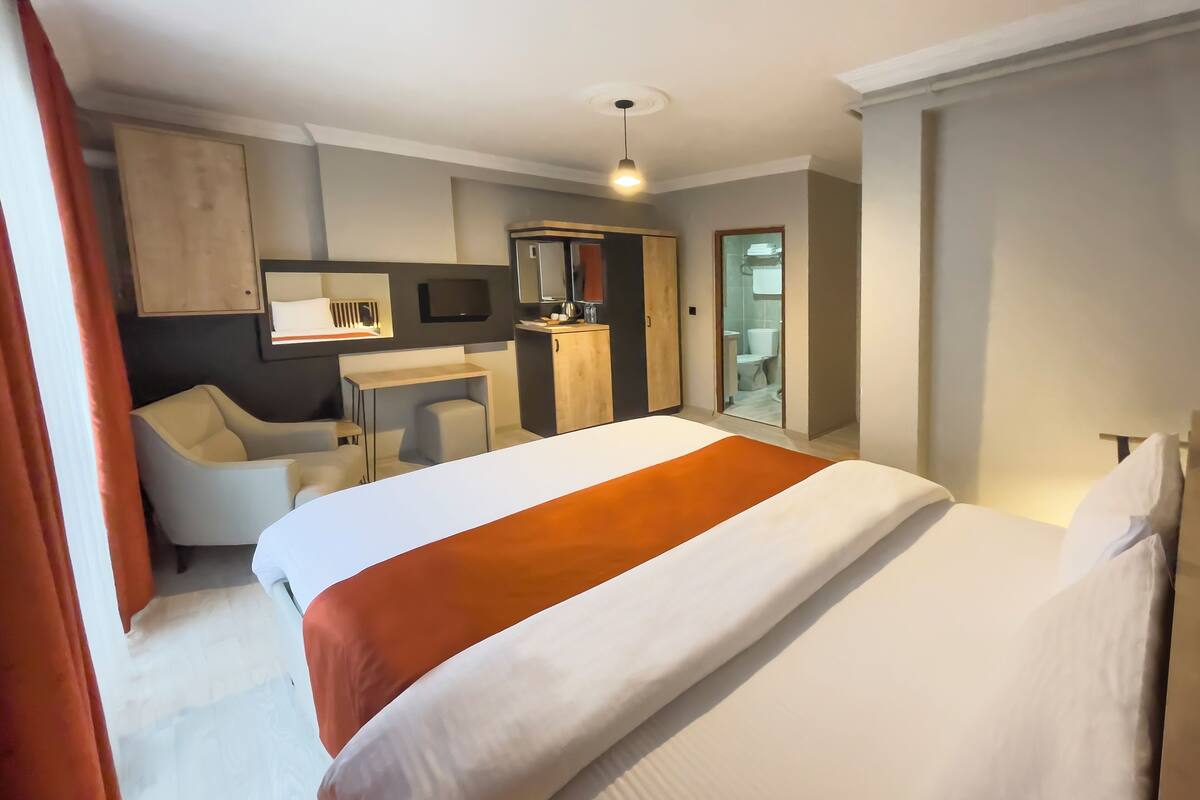 Habitación de hotel con cama, escritorio, silla, televisión y baño visible a través de una puerta abierta.