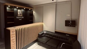 A reception area with a wooden reception desk, a black leather sofa, and a wall-mounted TV. - NEPTÜN INN (Kirklareli)