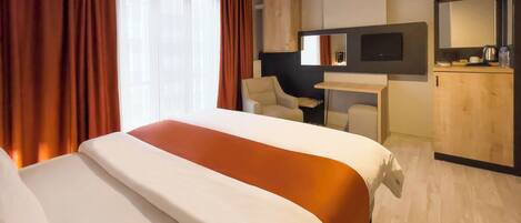 A hotel room with a large bed, a desk, a chair, a TV, and a mirror.
