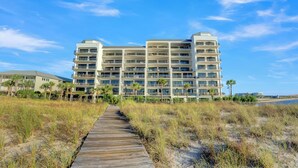 A multi-story hotel with a beach view, a boardwalk leading to the entrance, and a clear sky. - Grand Pointe 708 by Liquid Life (Orange Beach)