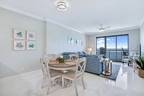 Ein geräumiges Wohnzimmer mit Esstisch, Stühlen, einer Couch und einem Balkon mit Meerblick.