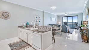 A modern kitchen with a central island, a dining area with a view, and a living space with a balcony. - Grand Pointe 708 by Liquid Life (Orange Beach)