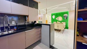A modern kitchen with a black countertop, stainless steel sink, and beige cabinets. There is a dining area with a green accent wall and a mirror.