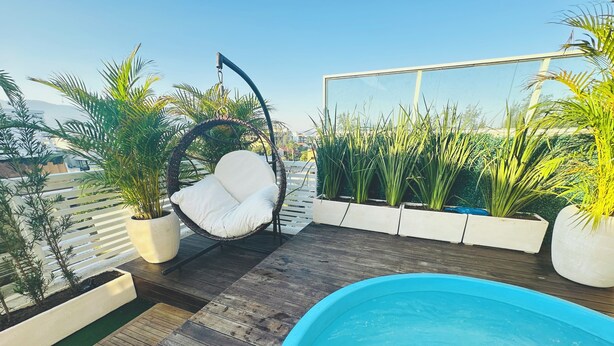A rooftop pool area with a hanging chair, potted plants, and a wooden deck.