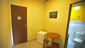 A small room with a wooden door, a small refrigerator, a wooden stool, and a painting on the wall. - colonial hotel de ilhabela (Ilhabela)