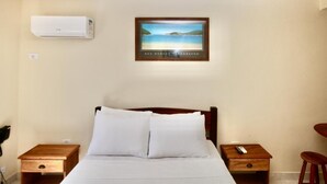 A hotel room with a bed, two wooden nightstands, a red chair, an air conditioning unit, and a framed photograph on the wall. - colonial hotel de ilhabela (Ilhabela)