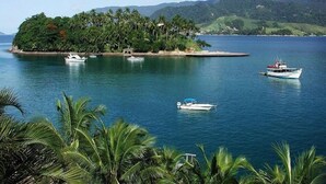 A tropical island with several boats anchored near the shore, surrounded by lush greenery and mountains in the background. - colonial hotel de ilhabela (Ilhabela)