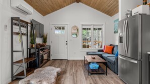 A modern kitchen with a wooden ceiling, a stainless steel refrigerator, a gray sofa, and a wooden coffee table. - New* Seabrook's Hammerbarn: Dog Friendly! (Pacific Beach)