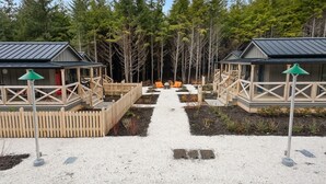 A pathway leading to two cabins with wooden decks and a forest backdrop. - New* Seabrook's Hammerbarn: Dog Friendly! (Pacific Beach)