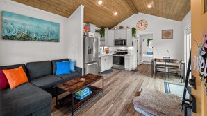 A modern living space with a gray sofa, a wooden coffee table, and a kitchen area featuring white cabinets and stainless steel appliances. - New* Seabrook's Hammerbarn: Dog Friendly! (Pacific Beach)