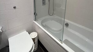Uma casa de banho moderna com chuveiro separado por vidro, uma banheira branca e uma sanita.