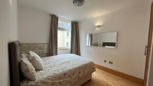 Quarto com cama, mesa de cabeceira, espelho e janela com cortinas.
