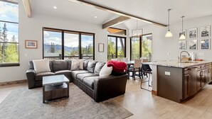 A modern living room with a sectional sofa, a coffee table, and a kitchen area with a countertop and sink.