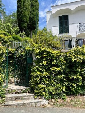 Un edificio blanco con entrada porticada, escalones de piedra y abundante vegetación.