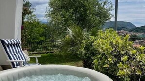 An outdoor hot tub with a person in it, surrounded by greenery and a view of a town and mountains in the background. - Villa with sea view Sestri Levante (Sestri Levante)