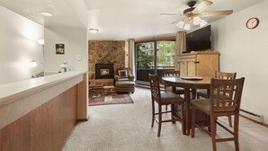 A kitchen with a stone backsplash, a dining area with wooden chairs, a ceiling fan, and a TV mounted on the wall. - Walk to the Marina and Amph in this central 2 BR Condo! (Dillon)