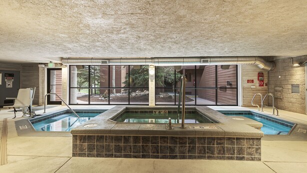 An indoor swimming pool with a stone-tiled hot tub area, large windows, and a view of the outdoors. - Walk to the Marina and Amph in this central 2 BR Condo! (Dillon)
