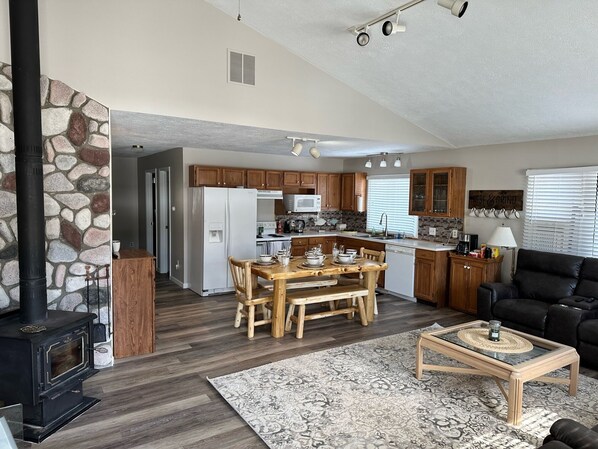 A spacious living area with a stone wall, a wooden dining table, a black leather sofa, and a kitchen with wooden cabinets and a white refrigerator. - Cozy house in Indian River. Walking distance to Burt Lake and the public Beach. (Indian River)