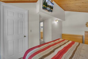 A bedroom with a bed, a television mounted on the wall, and a wooden ceiling.
