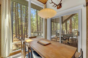 Ein Holzespeisesaal mit Stühlen, einer Hängelampe und Blick auf einen Wald durch große Fenster.