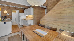 Cozinha com vigas de madeira, mesa de jantar com cadeiras e luminária pendente.