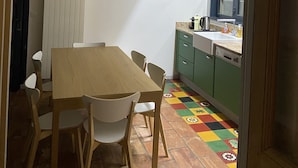 Een eetgedeelte met een houten tafel en stoelen, een schilderij aan de muur, en een keuken die zichtbaar is door een open doorgang.