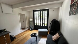Een knus woongedeelte met een bank, een klein tafeltje, een radiator, een deur naar buiten en een spiegel aan de muur.