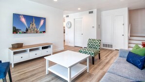A modern living room with a flat-screen TV, a white coffee table, a patterned armchair, and a grey sofa.