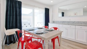 A dining area with a white table, red chairs, and a view of houses through the window.