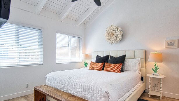 A bedroom with a large bed, a wooden bench, two bedside tables with lamps, and a decorative wall piece.