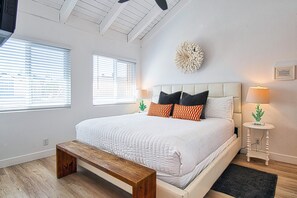 A bedroom with a large bed, a wooden bench, two bedside tables with lamps, and a decorative wall piece.