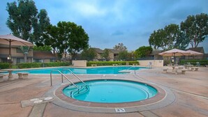 A swimming pool with a circular design, surrounded by a patio area with benches and umbrellas.
