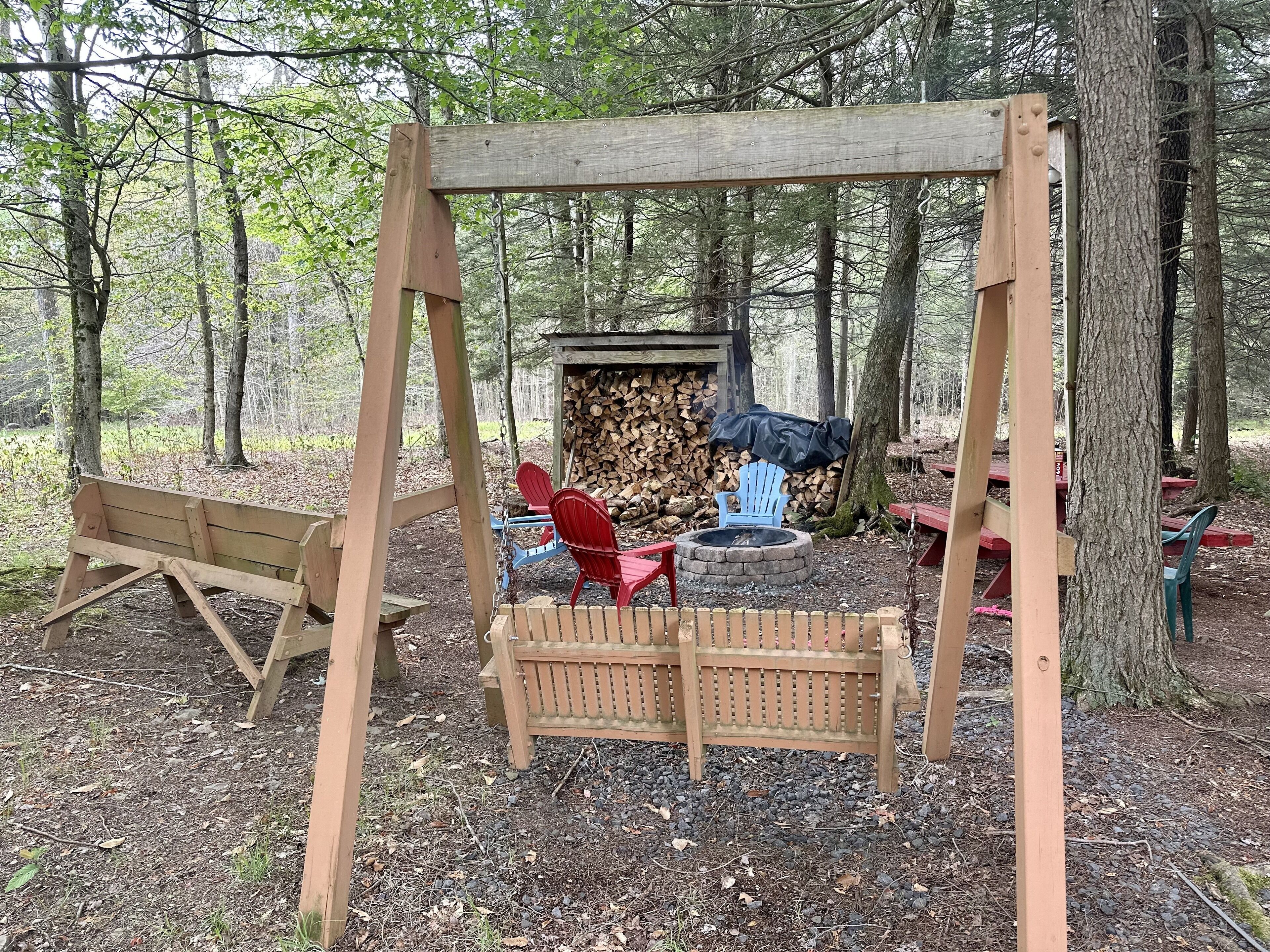 Un ensemble de balançoires en bois, un foyer et une pile de bois de chauffage, le tout installé dans un cadre forestier.