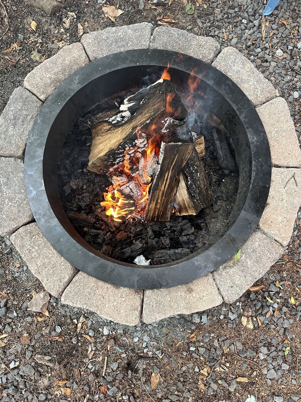 A circular fire pit with logs and flames, surrounded by stone bricks.