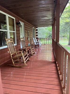 A wooden porch with rocking chairs and a table, overlooking a green landscape.