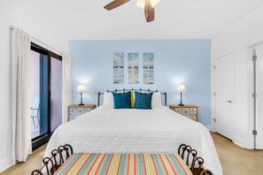 Un dormitorio con cama, dos mesitas de noche, ventilador de techo y una ventana con cortinas.