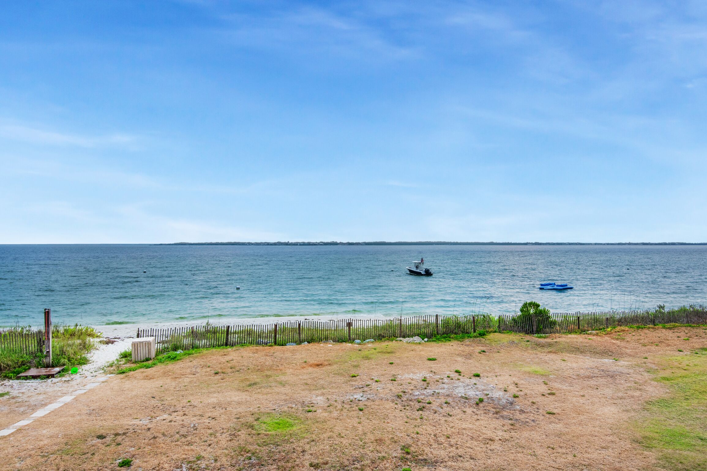 Een strand met een houten omheining, een zandpad en uitzicht op zee.
