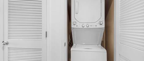 A compact laundry room with a washing machine and dryer, a door with louvered panels, and a vent on the ceiling.