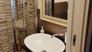 Ein modernes Badezimmer mit einer Duschkabine, einem weißen Waschbecken und einem großen Spiegel darüber.