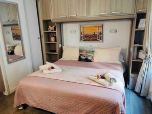 A neatly made double bed with pink bedding, a bedside table, a mirror, and a shelf with decorative items. - The Nest near Santa Croce (Firenze)