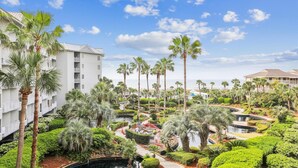 Resort com edifícios de vários andares, palmeiras e um jardim paisagístico com um espelho d'água.